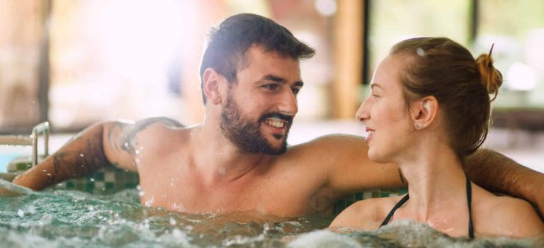 Happy couple enjoying bubble bath at wellness resort. Sun is shining through large windows.